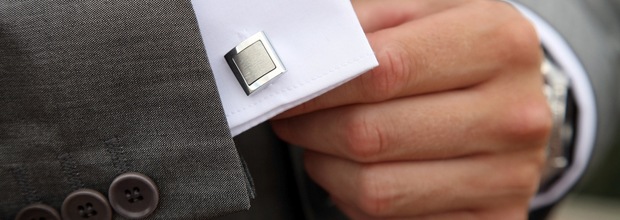 A man in a custom made suit fastening a cuff-link
