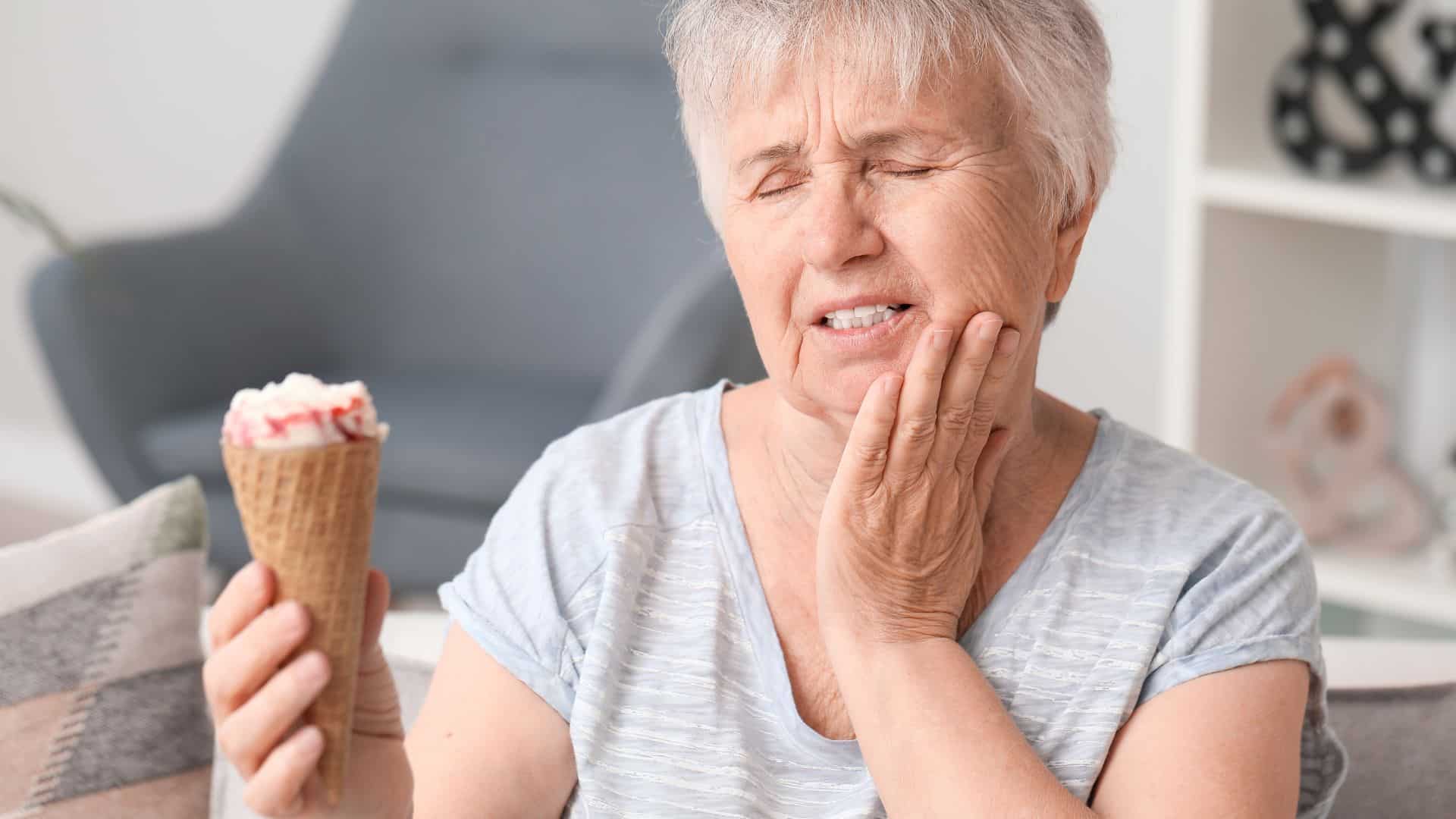 woman eating an ice cream cone holding her jaw because of tooth sensitivity