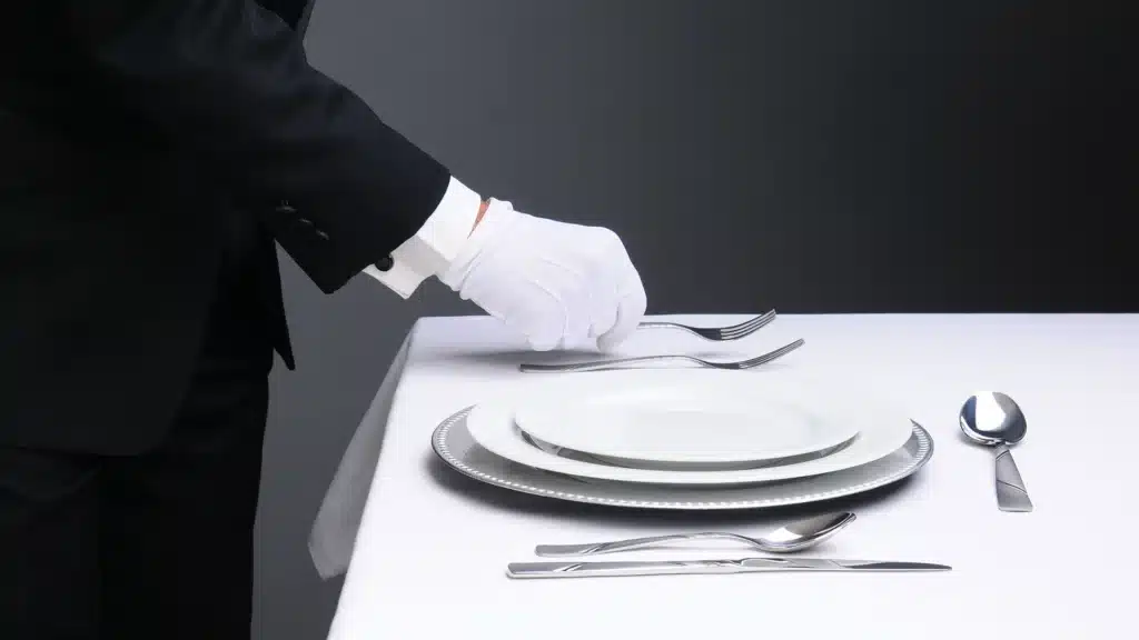 Closeup of a butler or waiter in a tuxedo setting a formal dinner table