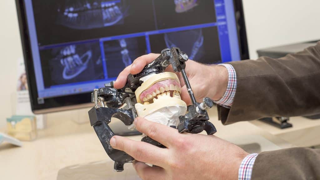 Close-up of a Dr. Drews holding a mounted dental model on a Combi II articulator, used to simulate jaw movement for denture planning.