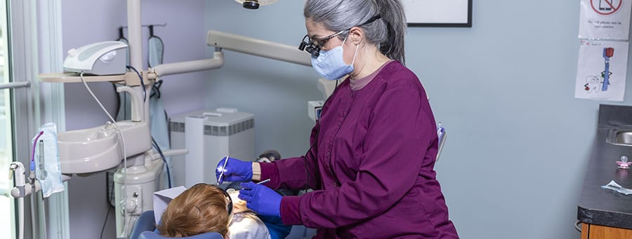 Dental hygienist performing a routine cleaning on a young patient in a treatment room at Drews Dental