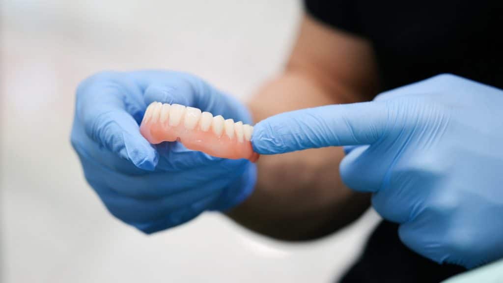 Dental professional holding an upper denture during patient care.