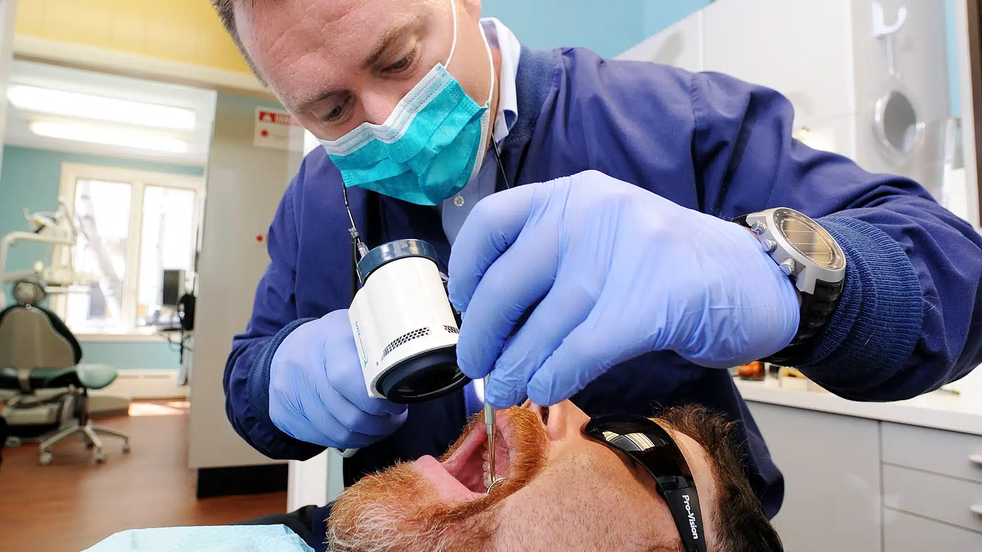 Dr. Drews looking into a patient's mouth with a VELscope enhanced oral cancer examination tool
