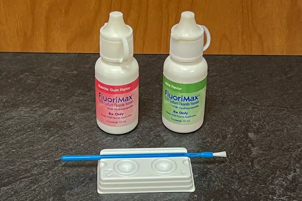 FluoriMax fluoride varnish bottles in mint and bubblegum flavors, with brush and mixing tray on counter