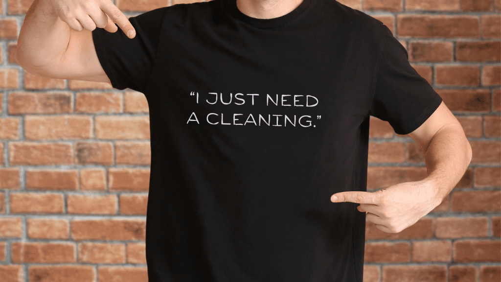 Person wearing a black T-shirt that reads “I just need a cleaning.”, illustrating a common assumption patients make before a dental exam.