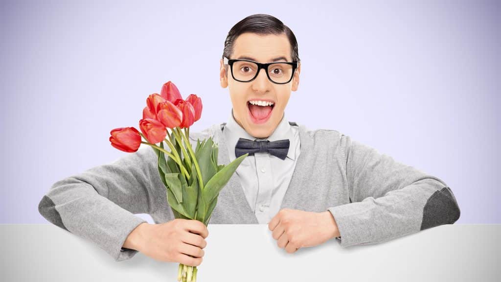 Smiling man holding flowers against a soft lavender background, representing sharing smiles and promoting oral health.
