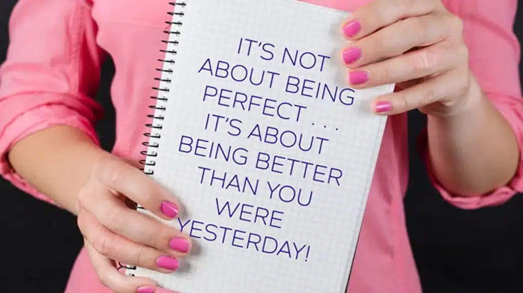 woman in a pink shirt holding a notebook that has a quote printed on it
