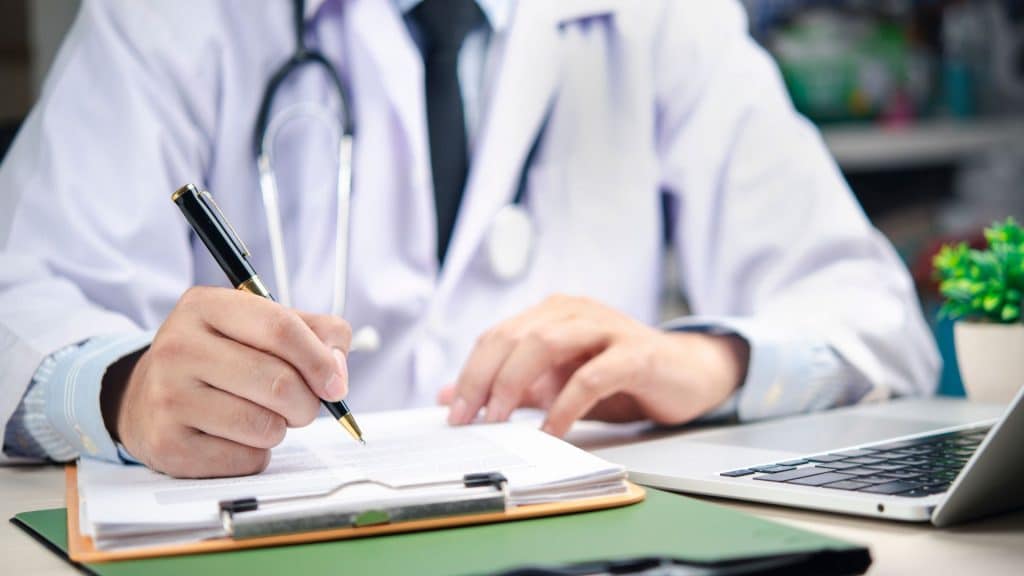 Medical professional reviewing and signing pre-surgical clearance documents during a patient evaluation