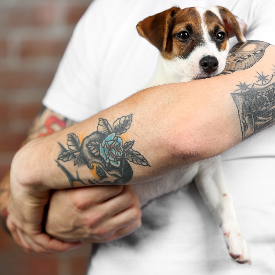 man with sleeve tattoos holding an adorable puppy