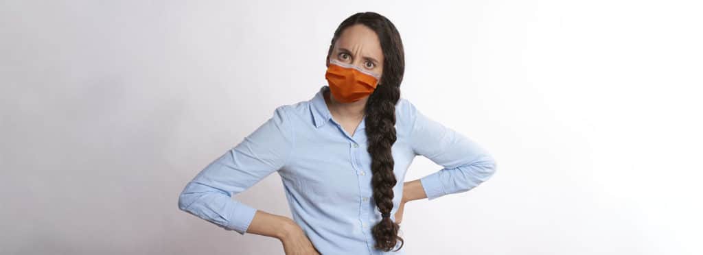 upset woman with her hands on her hips wearing an orange pandemic mask over her mouth and nose