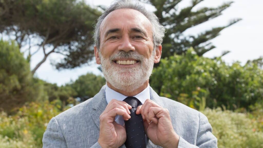 well-dressed man adjusting his tie and smiling confidently because of his high-quality dentures