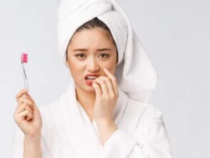 woman in a bathrobe holding a toothbrush worried about brushing her teeth